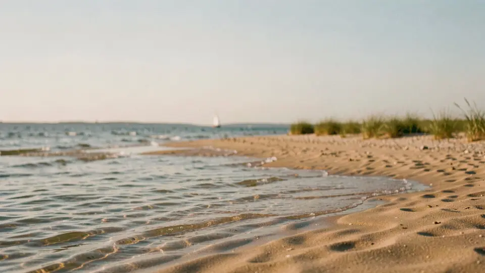 A wide, shallow warm bay at golden hour, glassy water, a pale sand beach curving away, a far wooded shore.