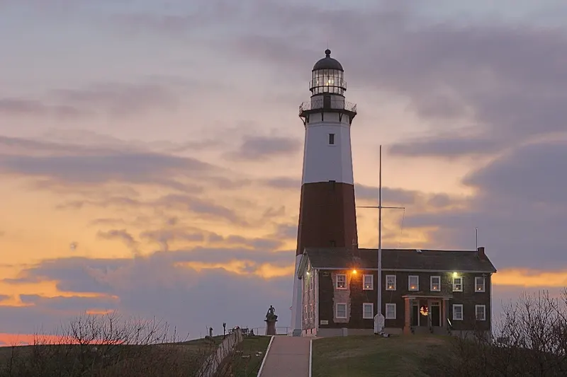 Montauk Point Lighthouse and the keeper's house at sunset with a lit lantern room.