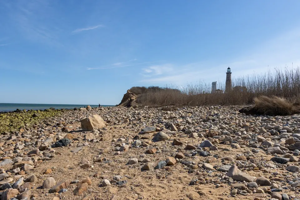 Rocky shore below the bluff with Montauk Point Lighthouse on the skyline.